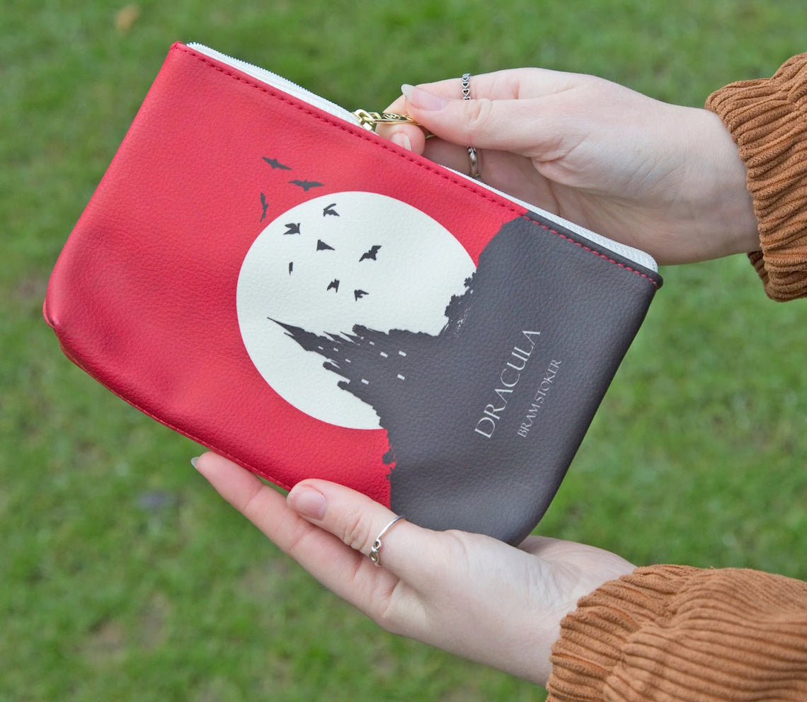 A person holding a red and black faux leather pouch with a white graphic of a castle and the text 'DRACULA'.