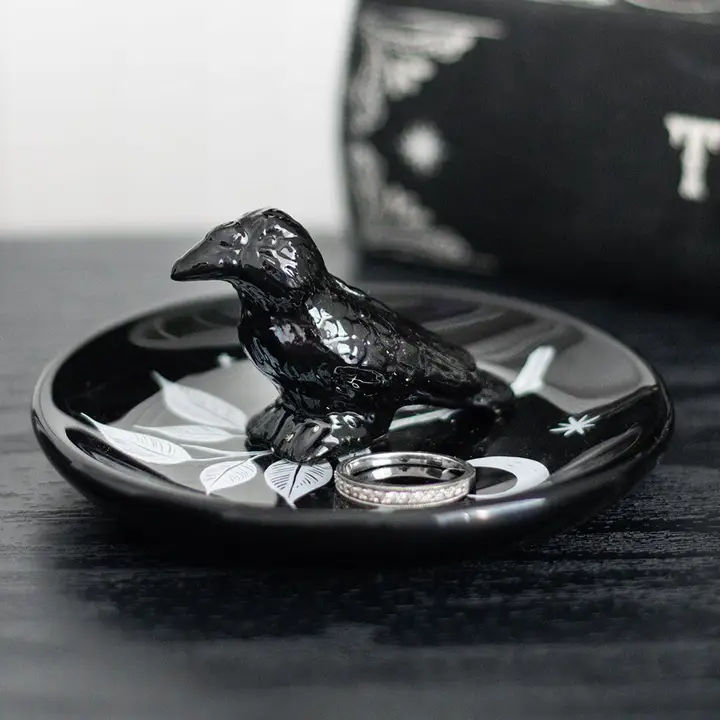 Black ceramic crow on a black dish with silver rings, against a blurred background.