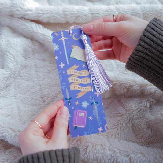 Hand holding a purple bookmark with tassel against a soft, light-colored fabric background