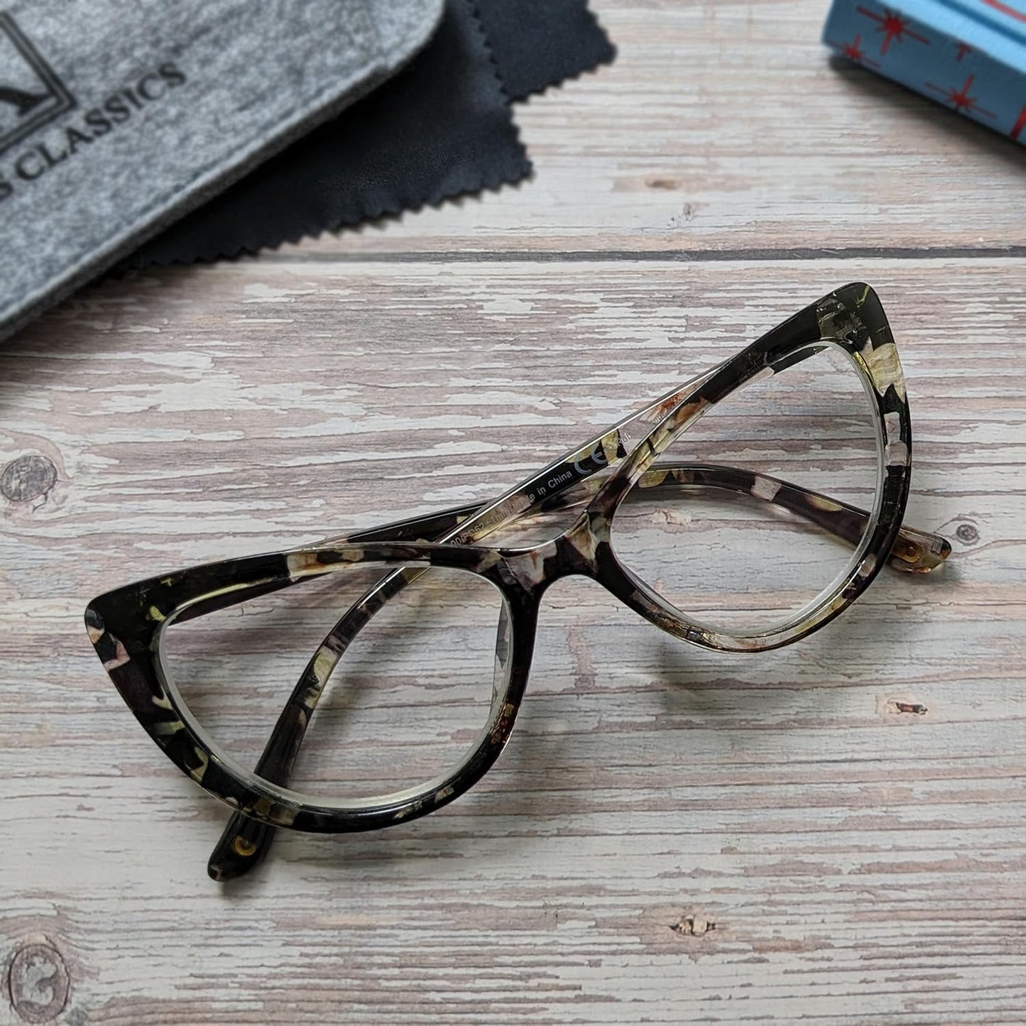 Tortoiseshell glasses on a wooden surface with a cloth and box in the background.