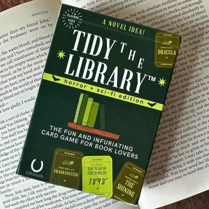 Card game packaging for 'Tidy the Library' on top of a book