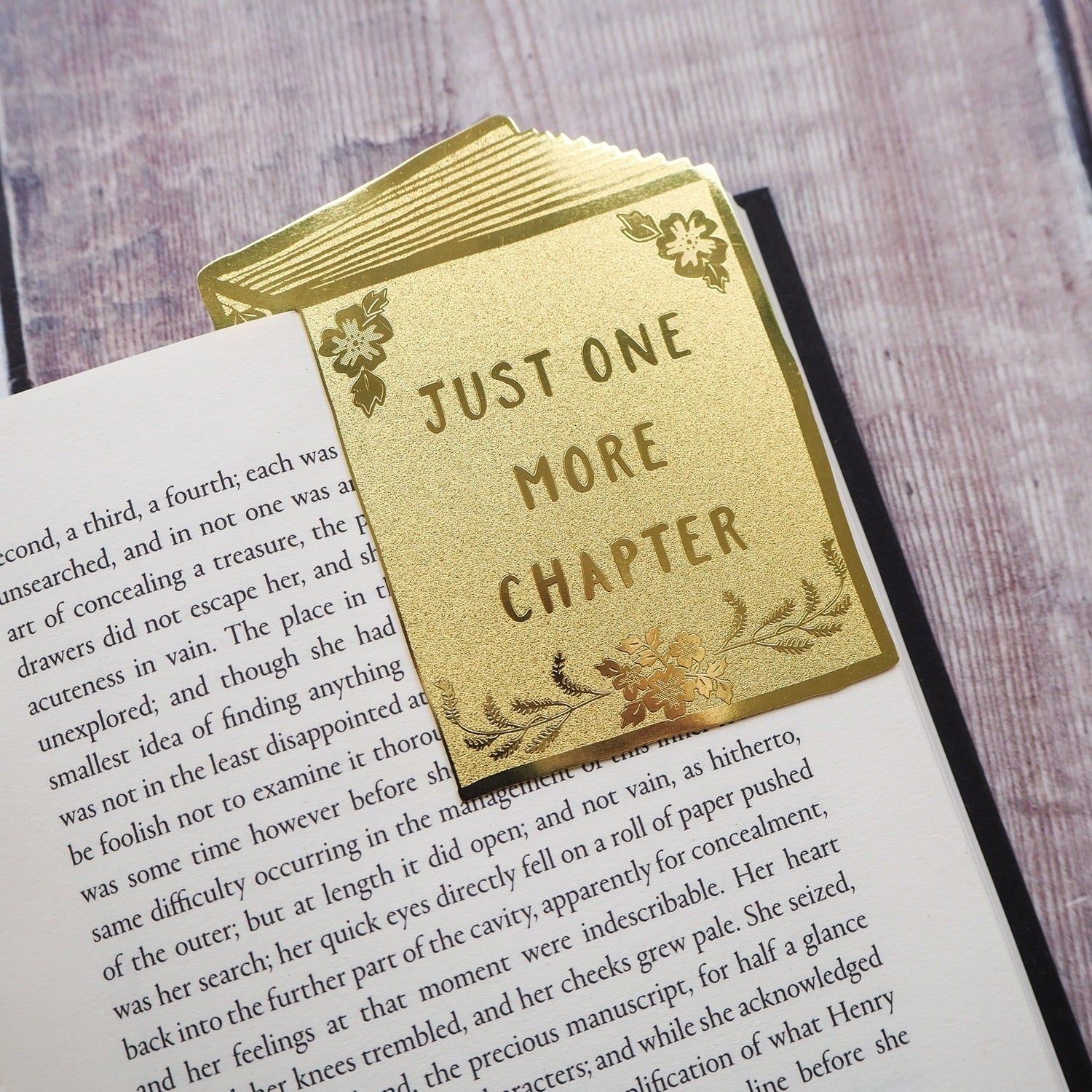 Just One More Chapter brass bookmark sitting on the corner of an open book