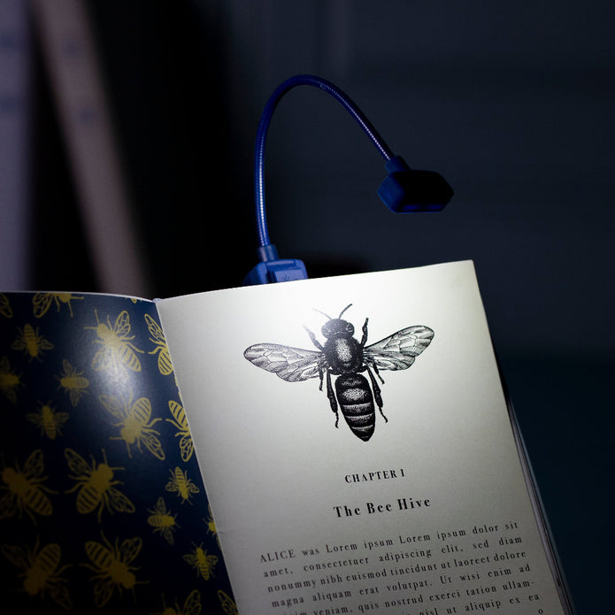 Open book with a bee illustration and a blue LED reading light on a dark background