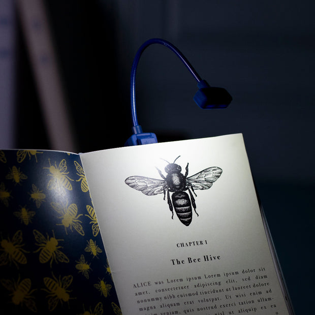 Open book with a bee illustration and a blue LED reading light on a dark background
