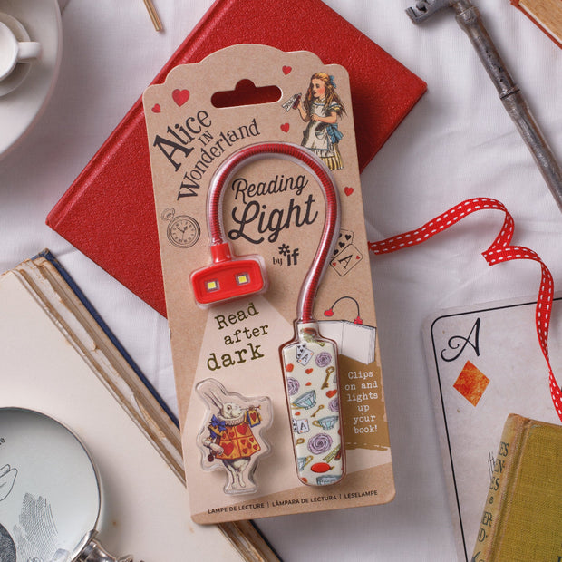 Reading light with 'Alice in Wonderland' theme packaging on a surface with books and a key.