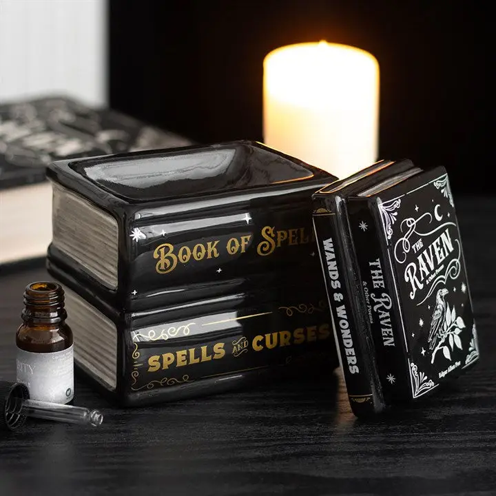 Decorative books shaped burner with mystical design, including 'Book of Spells' and 'The Raven', on a dark surface with a candle in the background.