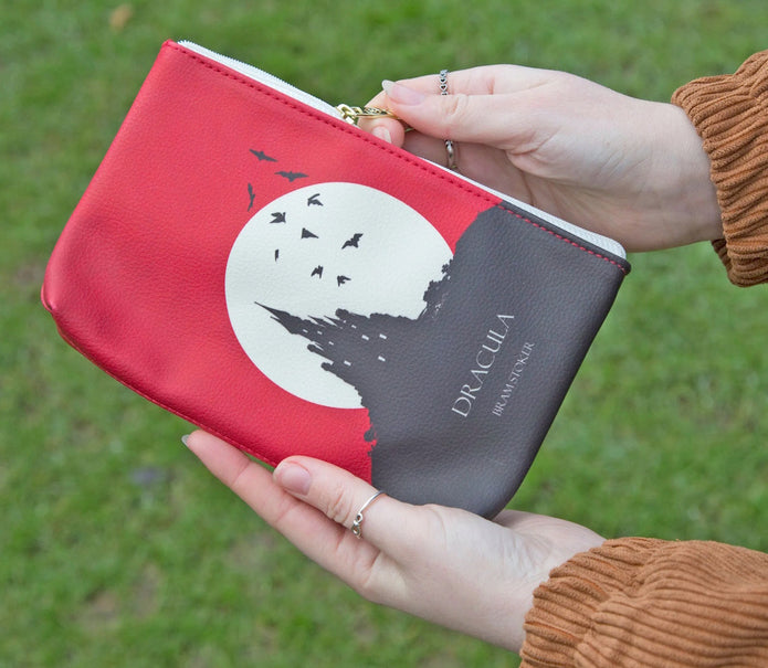 A person holding a red and black faux leather pouch with a white graphic of a castle and the text 'DRACULA'.