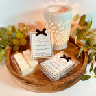 Wooden tray with wax melts, packaging, and a lit candle on a decorative background.