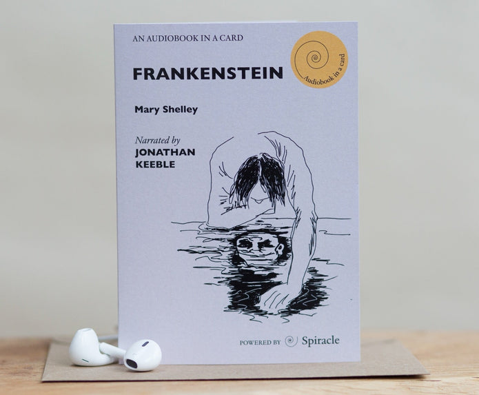 A single card-sized audiobook cover for Frankenstein by Mary Shelley, shown upright on a tabletop with two white earbuds resting in front. The cover is pale lavender with black text and line art of a woman reaching into water.