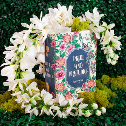 Book shaped vase titled 'Pride and Prejudice' surrounded by white flowers on a green background