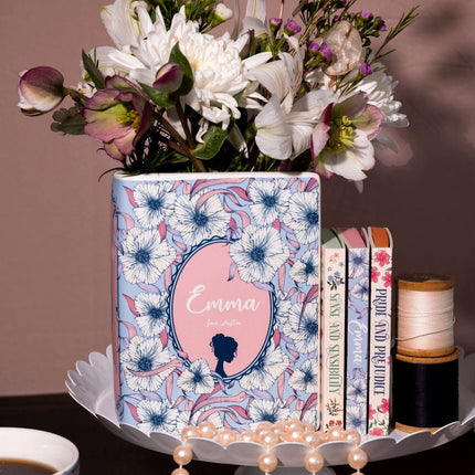 Decorative pot with floral design and text, placed on a stand with books and a cup of coffee.