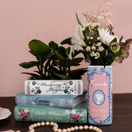 Decorative book shaped planters and vase with floral designs on a table against a pink wall.