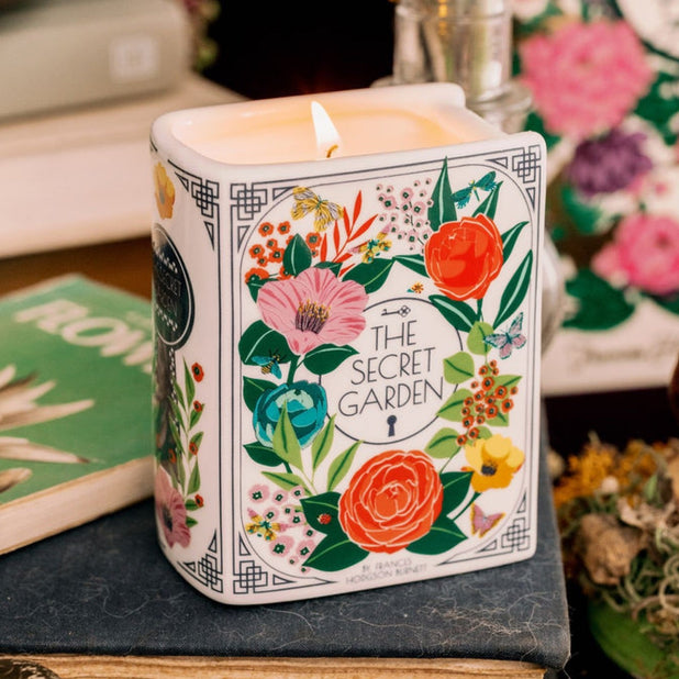 Candle with 'The Secret Garden' design on a book surrounded by decorative items