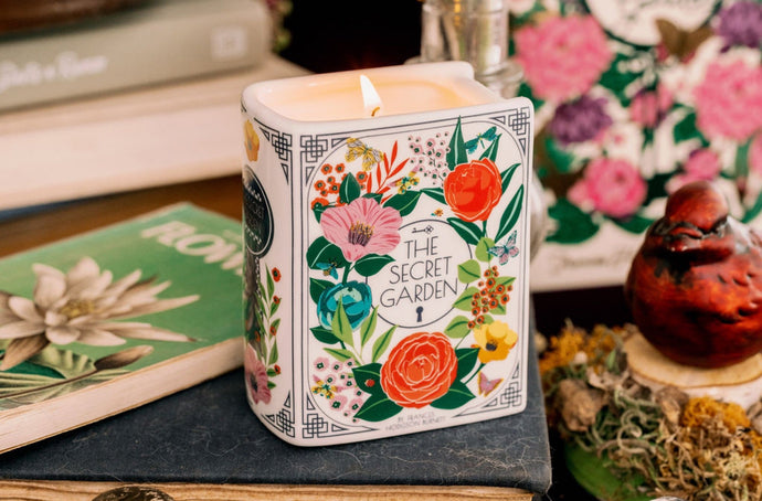 Candle with 'The Secret Garden' design on a book surrounded by decorative items