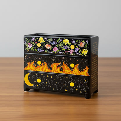 Black planter with floral and fiery designs on a tabletop