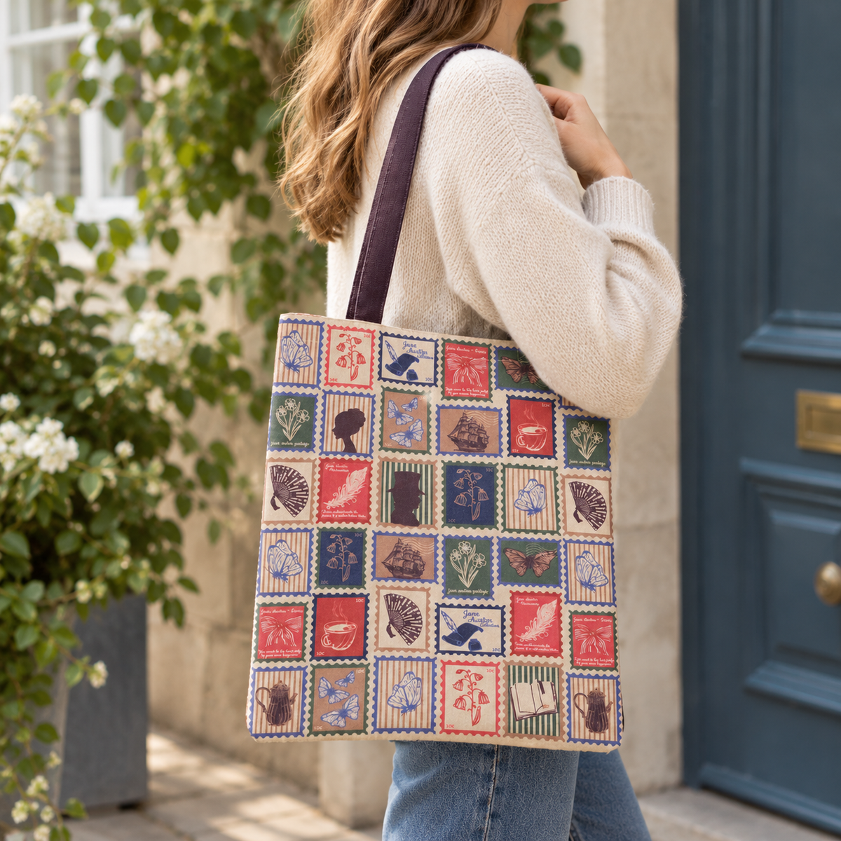 A woman wearing a cream knit sweater and blue jeans carries a large rectangular patchwork tote bag with brown straps. The tote bag features a grid of colourful stamp motifs including birds, leaves, animals, and small illustrations.