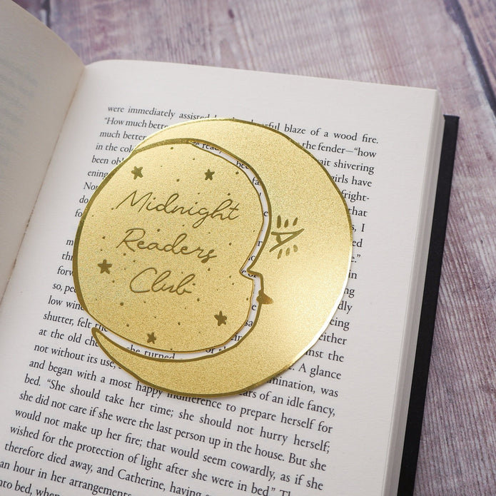 Gold 'Midnight Readers Club' bookmark on an open book