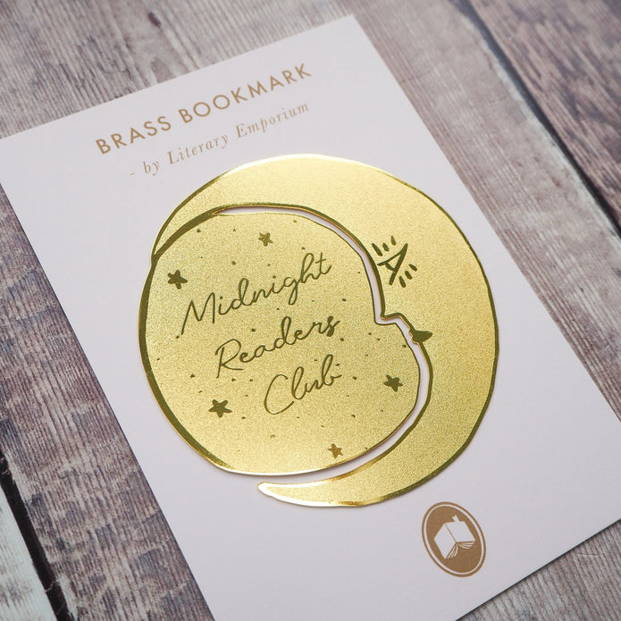 Gold brass bookmark on a white card with 'Midnight Readers Club' text, on a wooden surface.