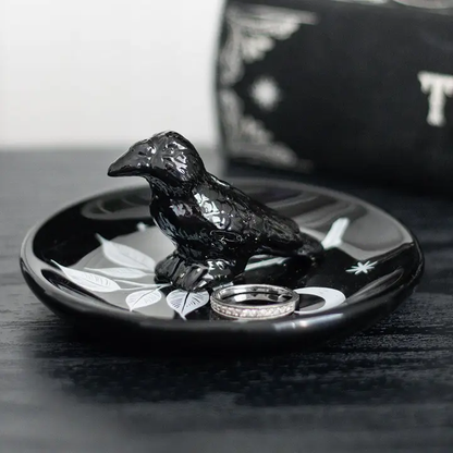 Black ceramic crow on a black dish with silver rings, against a blurred background.