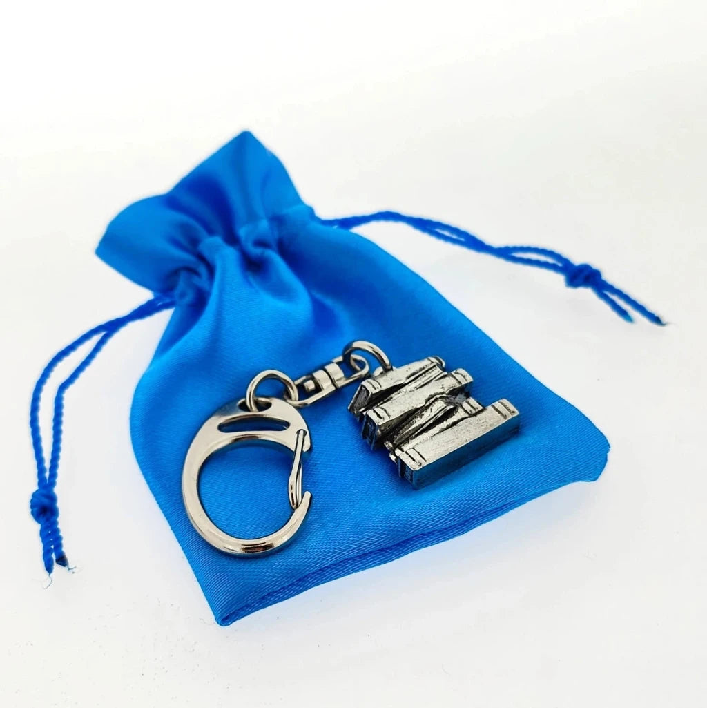 A silver-toned metal keychain with a small rectangular charm, displayed on top of a small blue drawstring pouch against a white background.