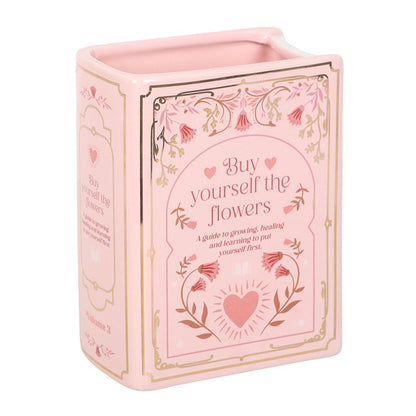 Pink book shaped vase with floral design and text on a white background