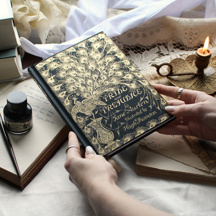 Person holding a book titled 'Pride and Prejudice' with decorative cover on a table.