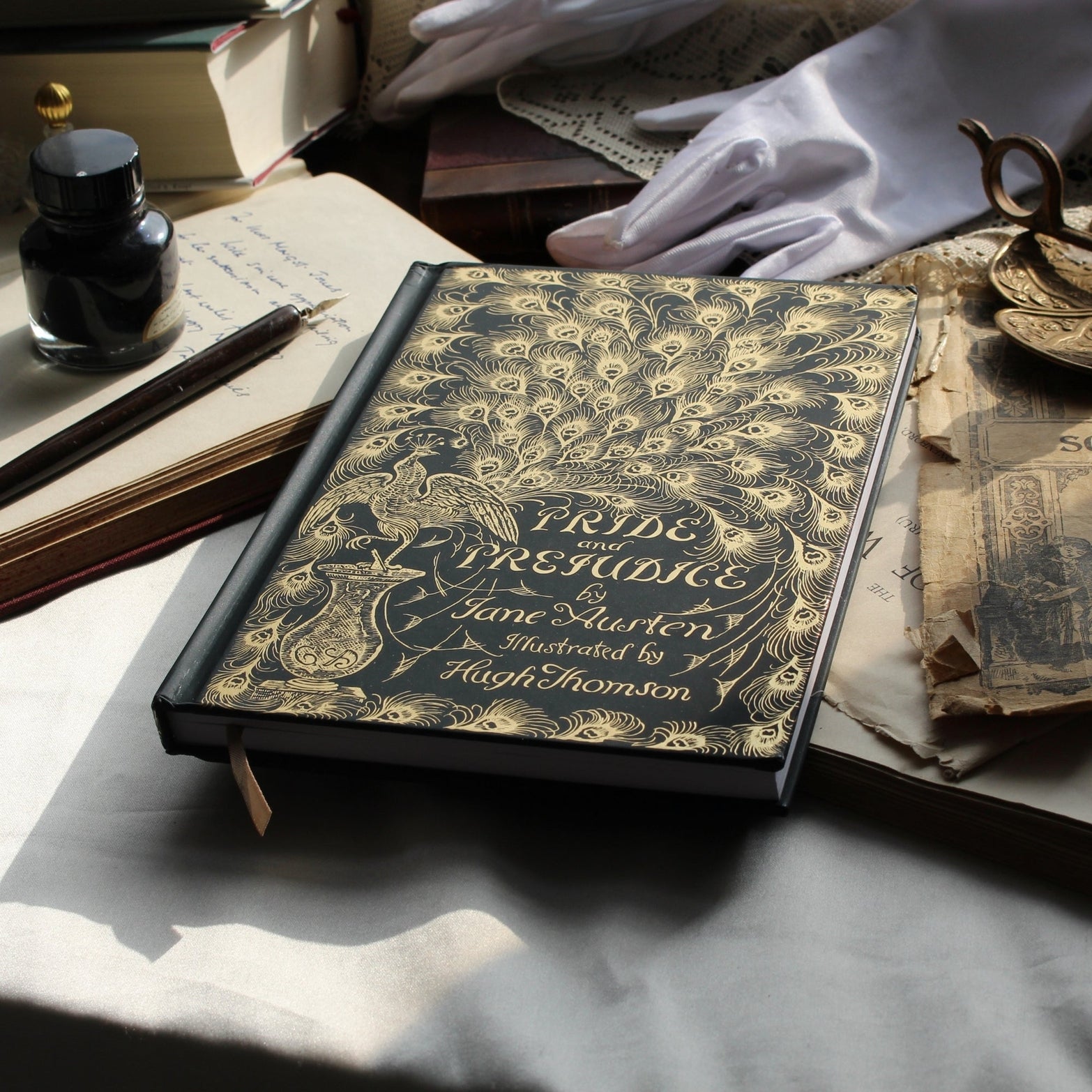 Vintage book titled 'Pride and Prejudice' by Jane Austen on a table with gloves and inkwell.