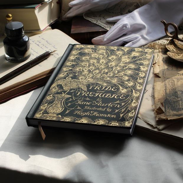 Vintage book titled 'Pride and Prejudice' by Jane Austen on a table with gloves and inkwell.