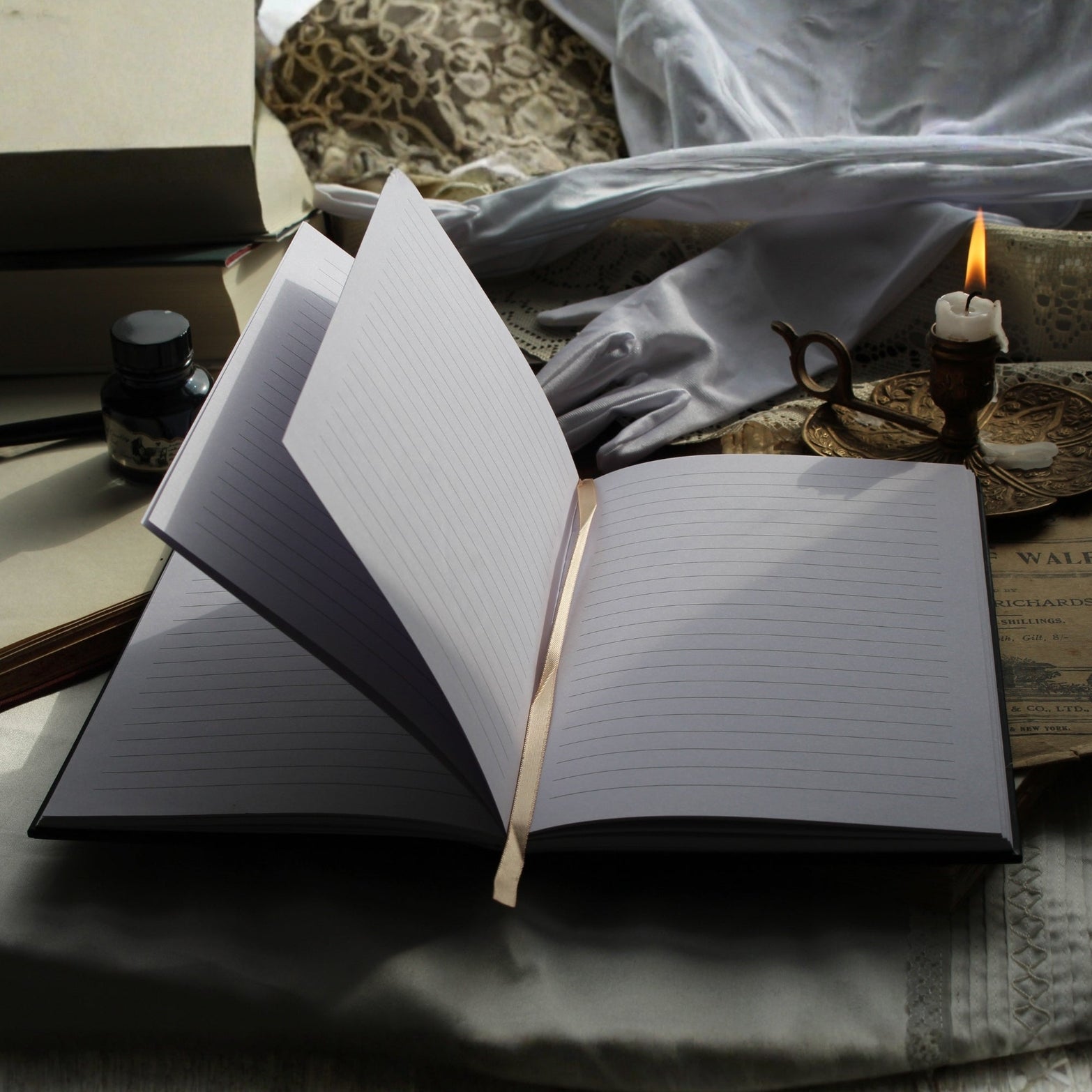 Open notebook on a textured surface with a candle and gloves in the background