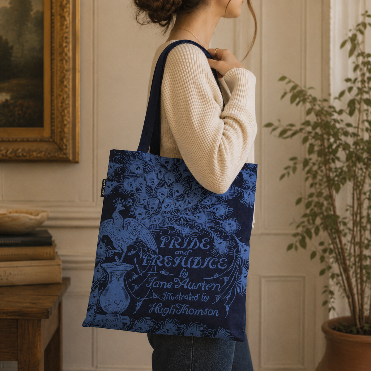 Person holding a blue tote bag with 'Pride and Prejudice' design in an indoor setting.