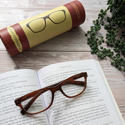 Brown eyeglasses on an open book with a cylindrical product packaging in the background.