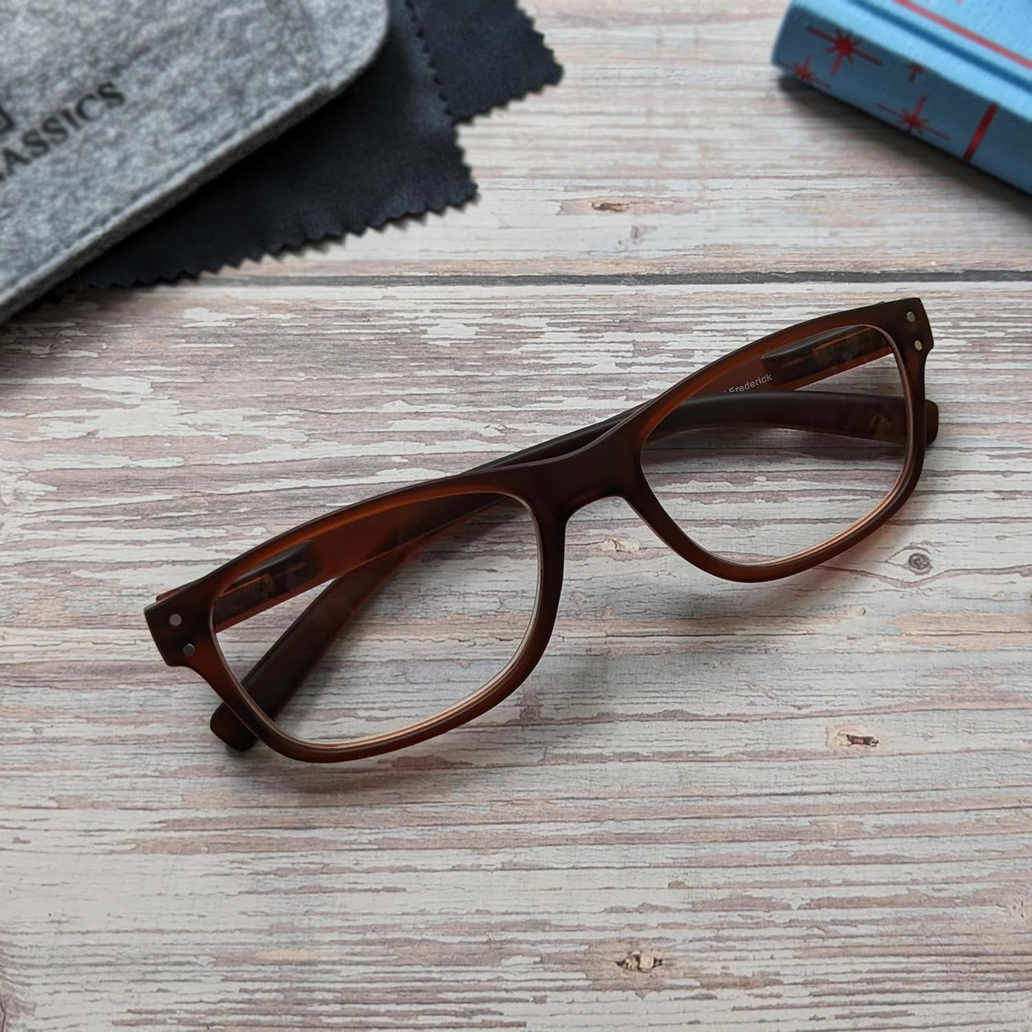 Brown eyeglasses on a wooden surface with a cloth and book in the background