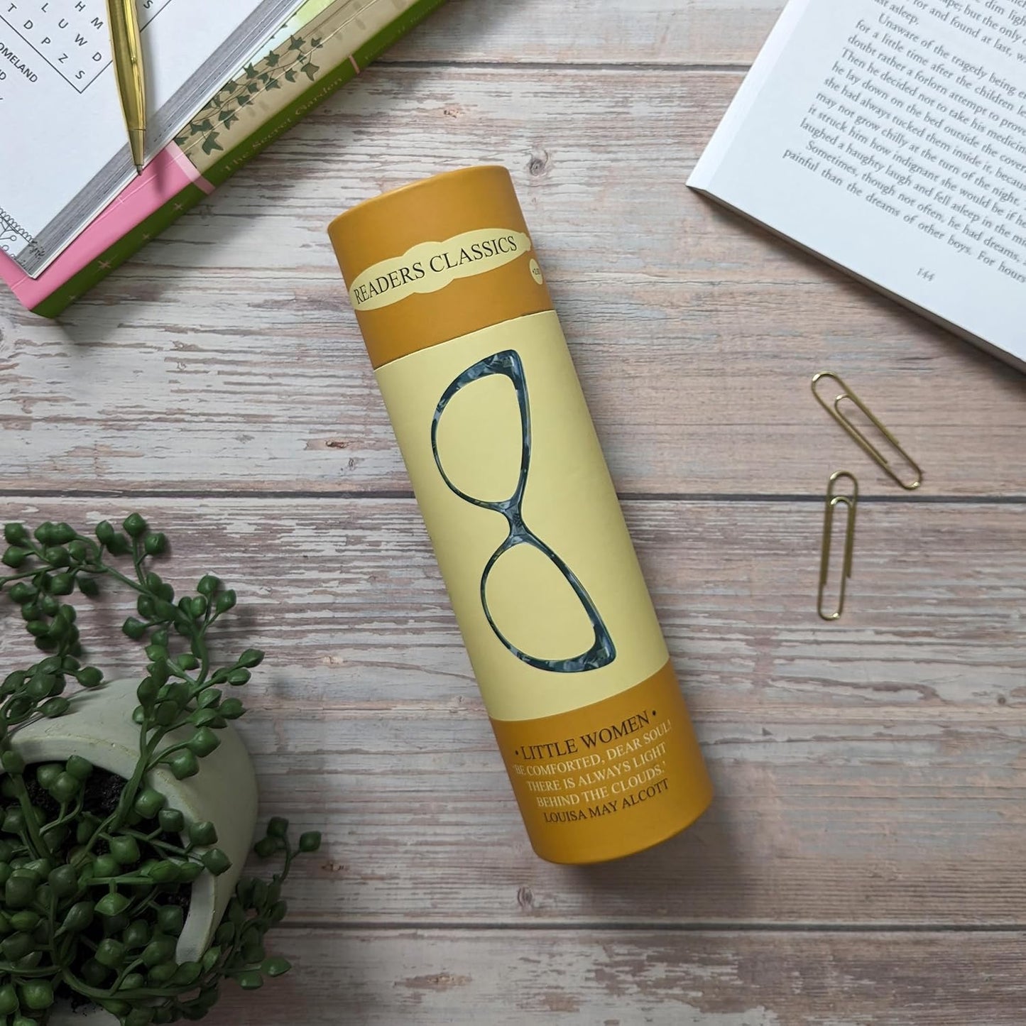 Yellow penguin book style tube with 'Little Women' on a wooden surface with books and a plant.