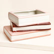 Stack of ceramic containers with rose gold accents on a light background