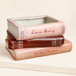 Stack of decorative books with 'Love Story' and 'All About The Books' text on a beige background