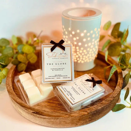 The Globe Wax Melts on a tray on a table with a lit candle and leaves in the background.