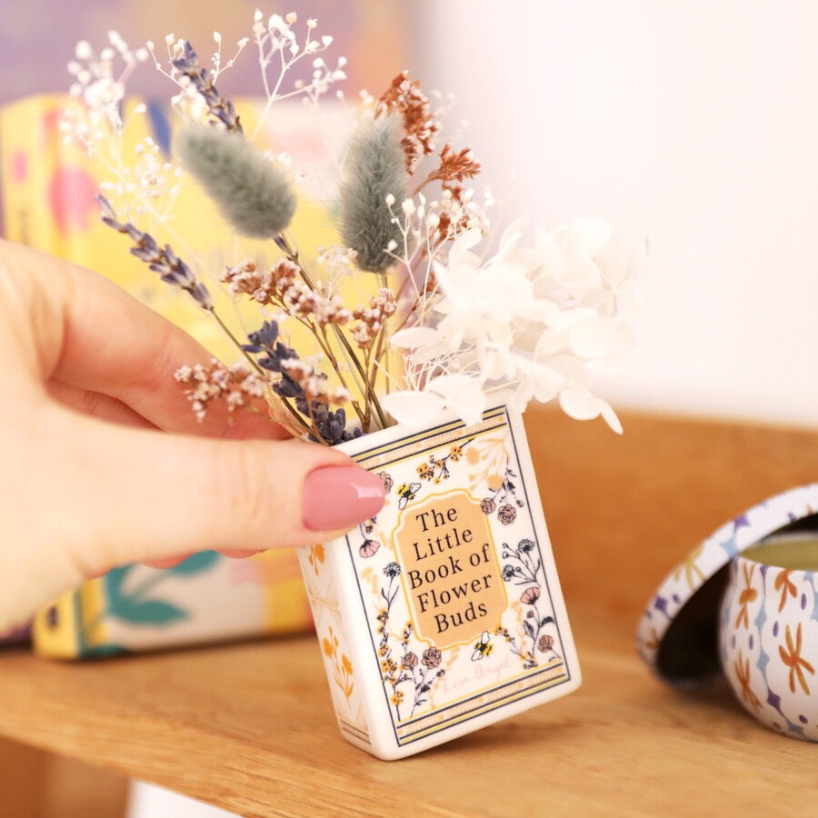 Small decorative vase with flowers inside a book-shaped container on a wooden surface.