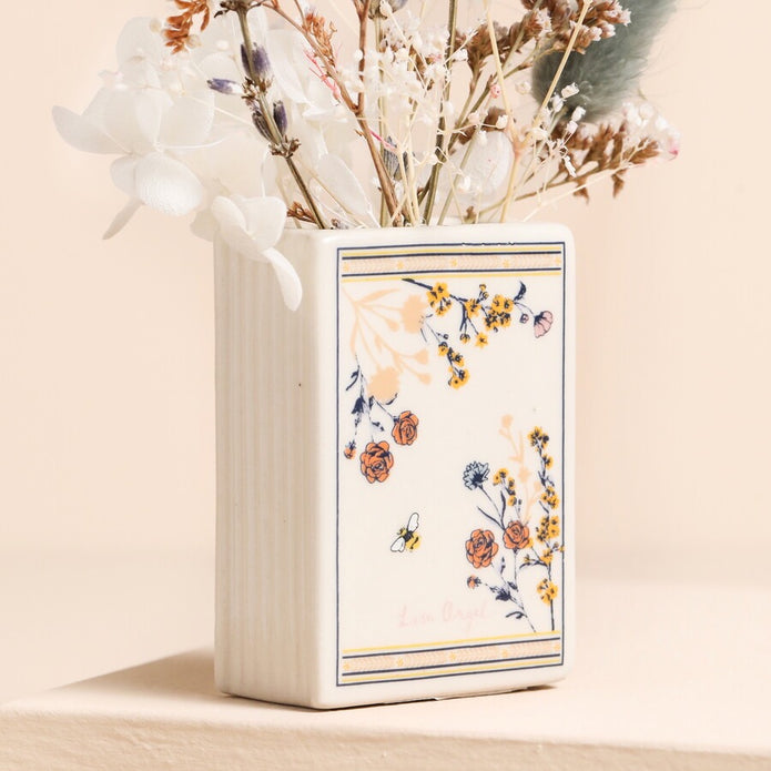 Decorative vase with floral design holding dried flowers on a beige background