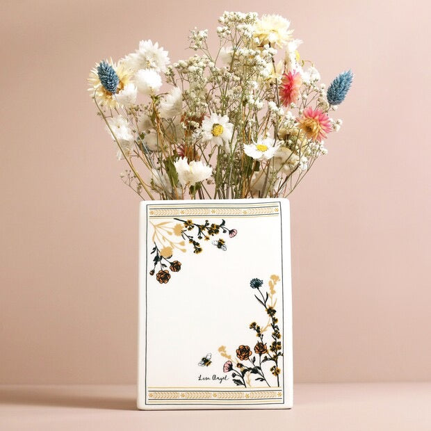 Bouquet of dried flowers in a white vase with floral design on a pink background