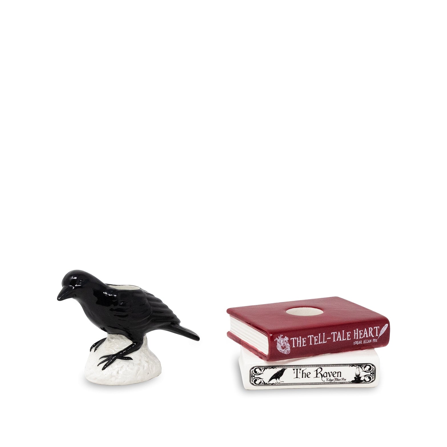 A black raven figurine perched on a white rock base, shown beside two miniature books from The Tell-Tale Heart: a red book labeled 'The Tell-Tale Heart' and a white book labeled 'The Raven'.