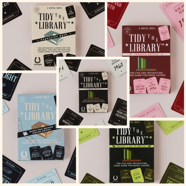 A collage of multiple Tidy the Library expansion packs and cards arranged on a pale pink background. The packs include Romance, Fantasy, Sci-Fi/Fuel Pits, Historical, and Contemporary/Fiction/Non-Fiction versions, each with different colored boxes and matching cards.