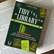 Card game packaging for 'Tidy the Library' on top of a book