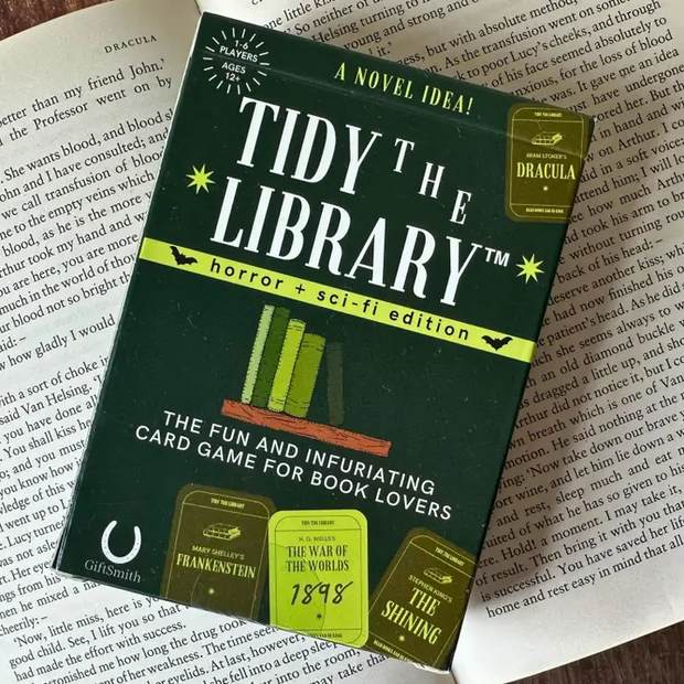 Card game packaging for 'Tidy the Library' on top of a book