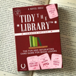 Card game box titled 'Tidy the Library' on top of a book