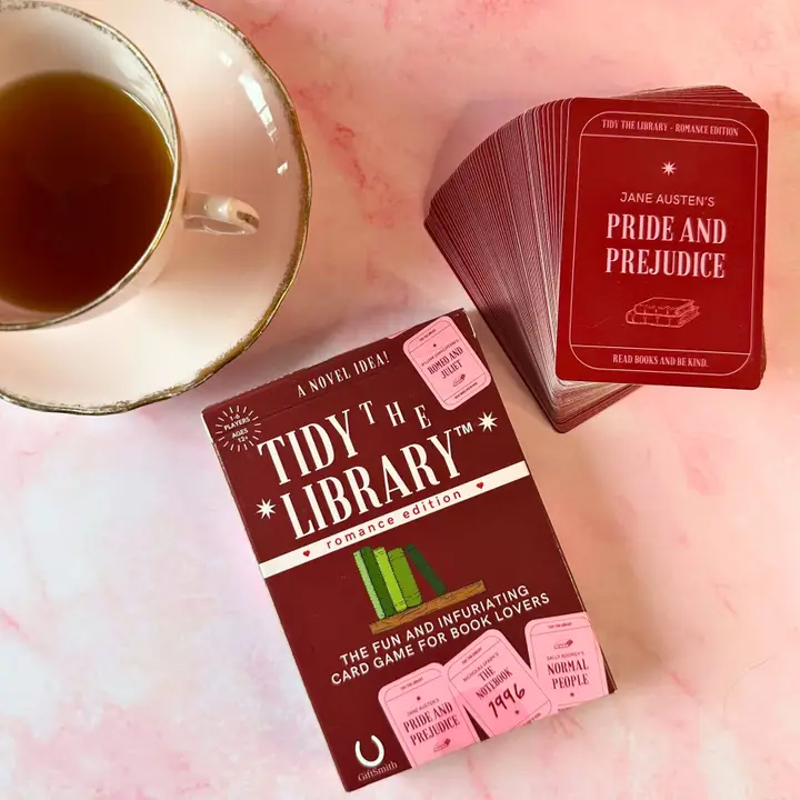 Tidy the Library card game and cards on a pink surface with a cup of tea.