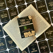 The image shows the card game 'Tidy the Library' laid out on an open book. The game includes a rulebook, library cards, and book cards with various book titles.
