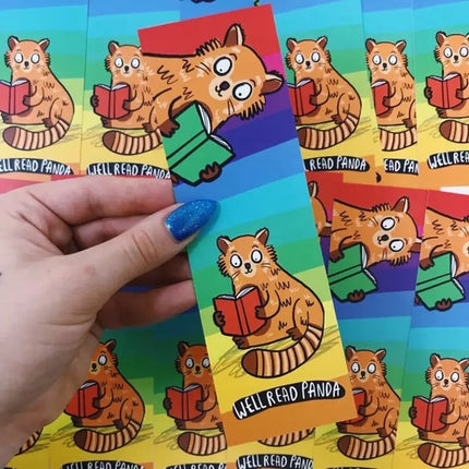 Colourful bookmark with a cartoon panda reading a book, held by a hand against a background of similar bookmarks.