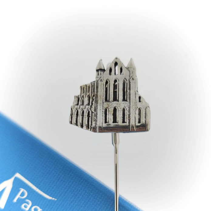 A small silver-toned metal bookmark shaped like a gothic cathedral or historic building, shown close up against a white background with a blue branded card partially visible at the lower left.