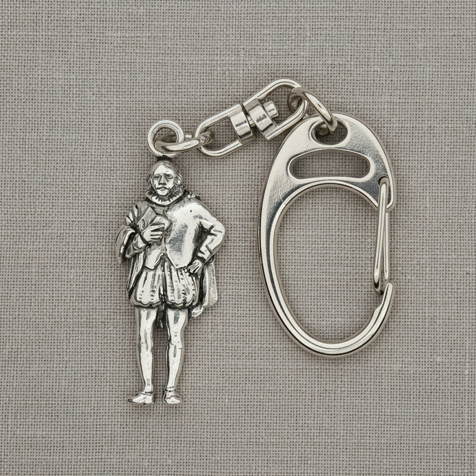 A silver-tone metal keychain featuring a detailed miniature figure of a historical man in Renaissance clothing, attached to a carabiner clip, displayed on a bright blue satin fabric background.