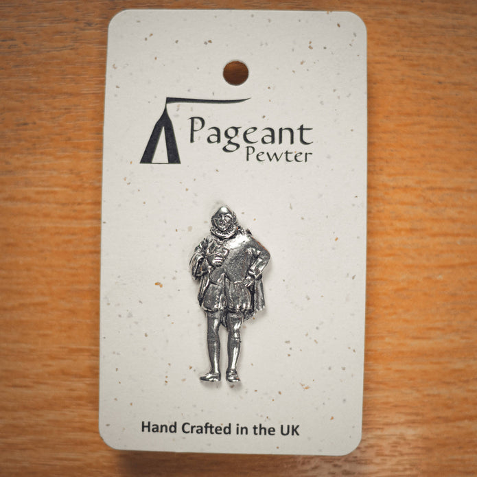A silver pewter pin of a William Shakespeare, mounted on a speckled white display card from the brand Pageant Pewter, placed on a wooden surface.